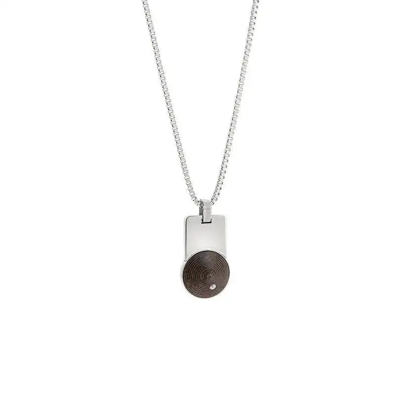 A silver necklace with a rectangular pendant featuring a circular, dark wood inlay and a small round accent.