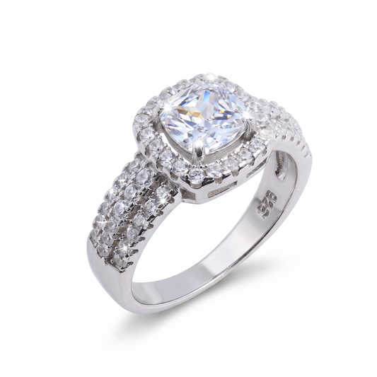 The Raelynn sterling silver engagement ring showcases a cushion-cut central gemstone, encircled by smaller clear stones and complemented by a band adorned with additional clear stones.