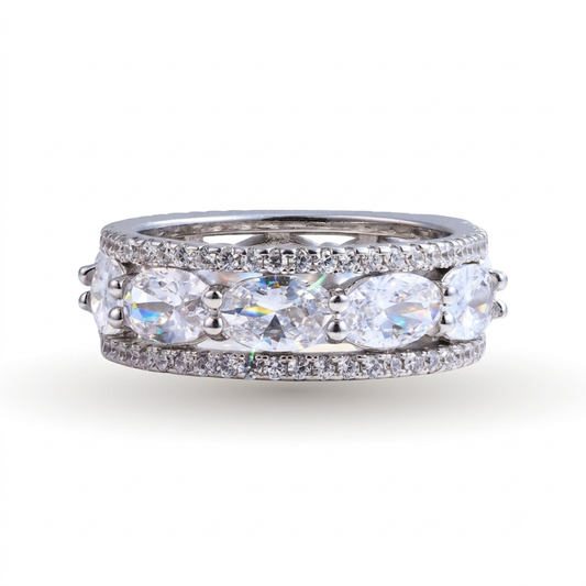 The Constantia sterling silver wedding band is displayed on a white background and features a row of large oval-cut clear gemstones set between two rows of small round gemstones.